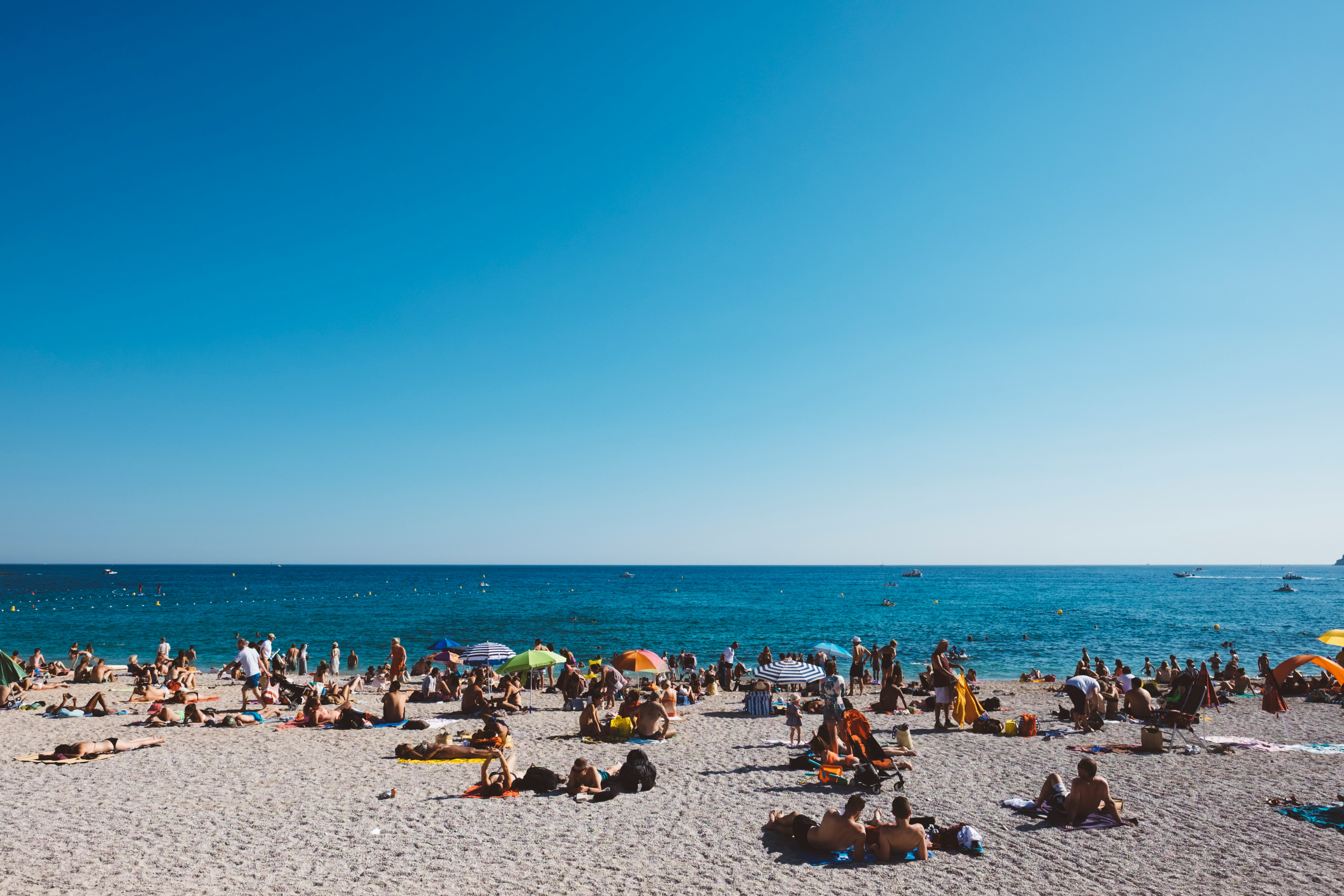 group of people enjoying the gray sanded beach with calm water during daytime